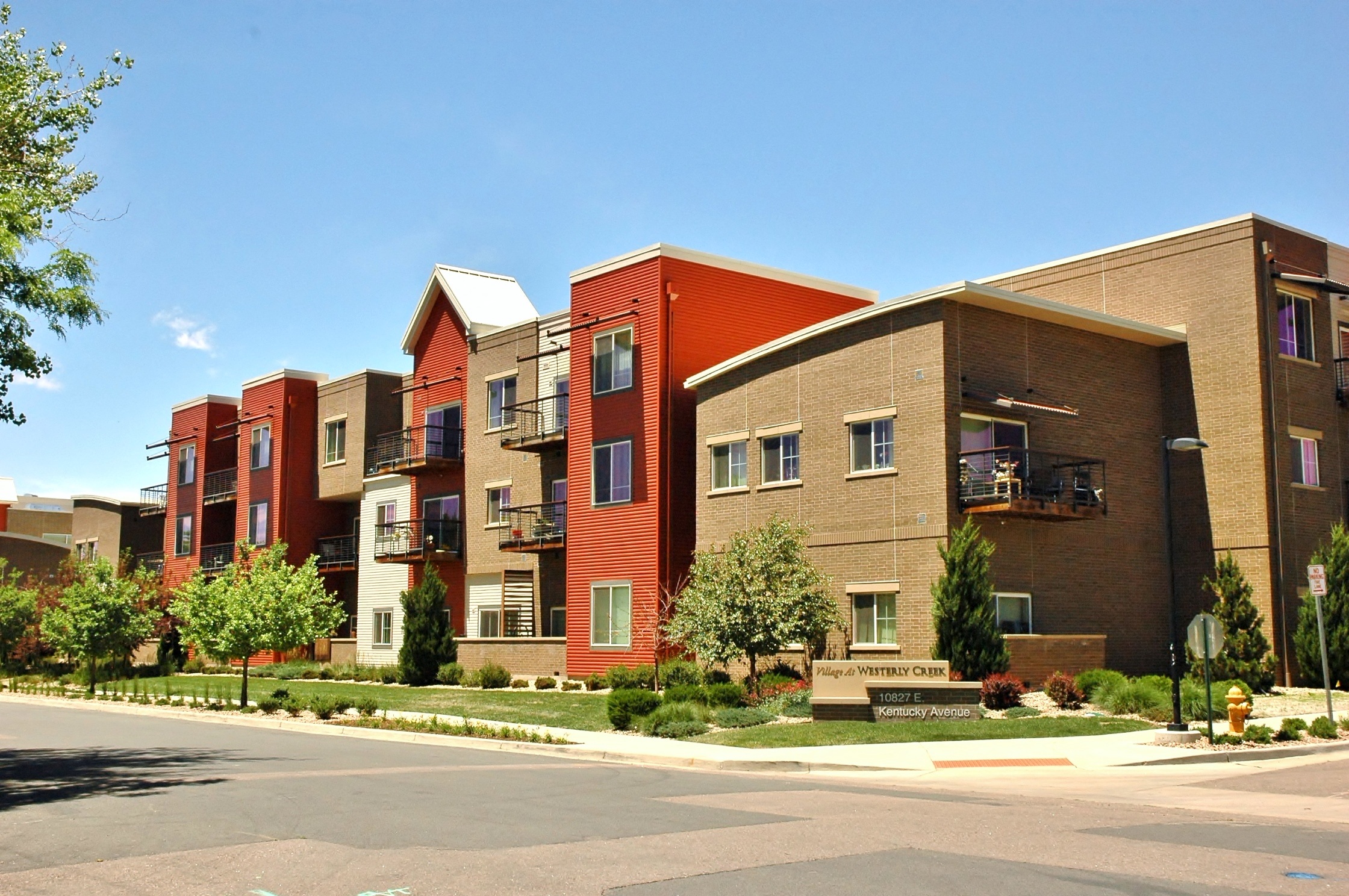 Exterior shot of VWC1, brown brick, orange siding, patios, landscaped with trees and grass